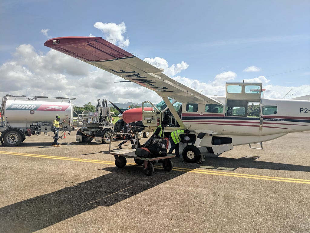 Small plane with a person loading luggage into the bottom compartment.