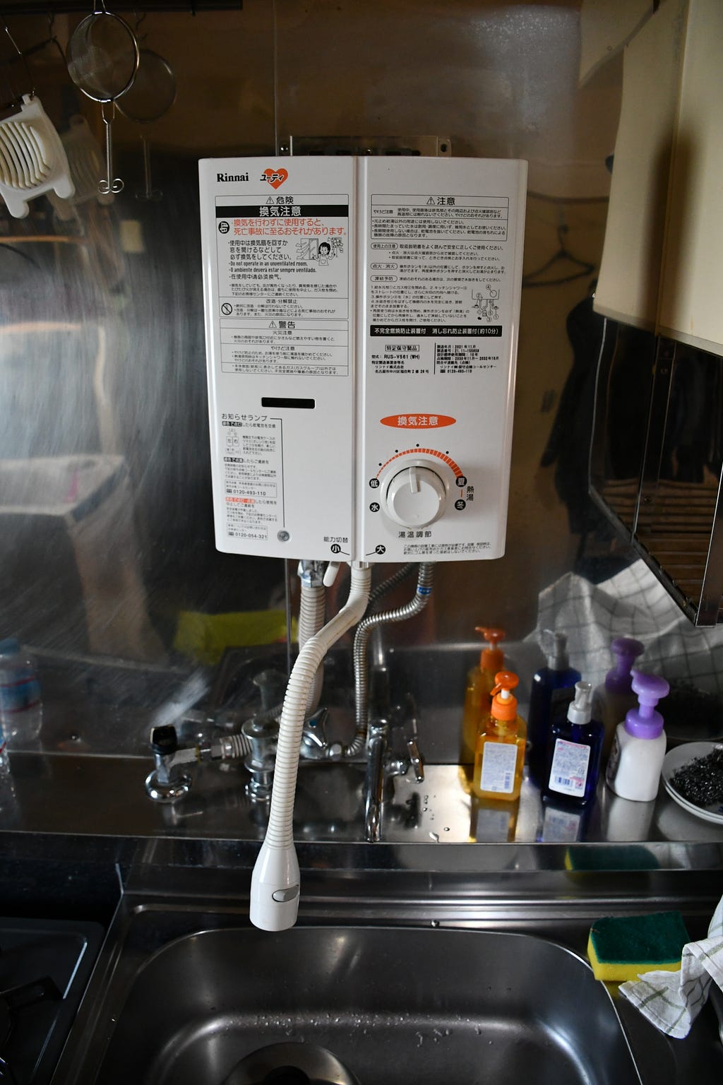 A tankless water heater mounted over the kitchen sink in Japan