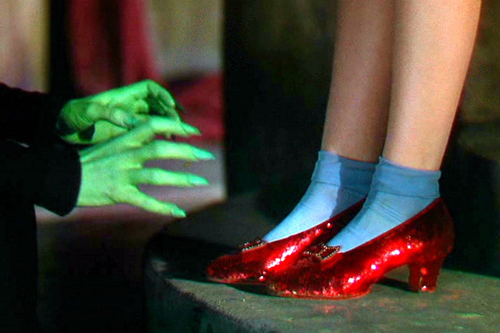 A scene from the movie the Wizard of Oz with the bright red slippers on Dorothy, as the witch’s green hands reach towards them.