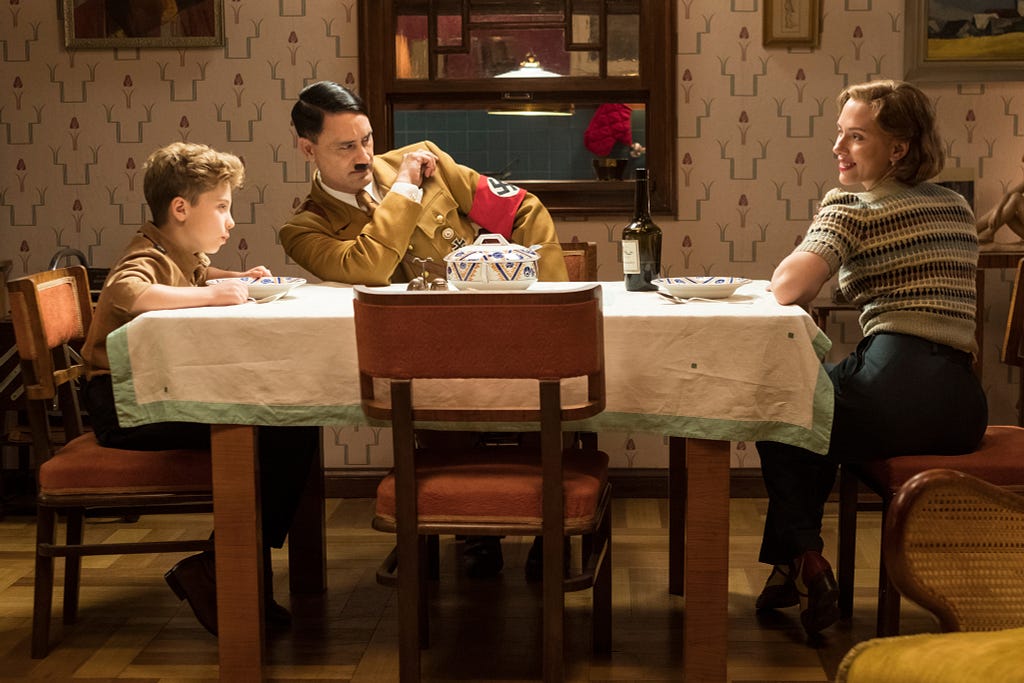 Scene from Jojo Rabbit: Jojo and his mom at the dinner table, along with Hitler.