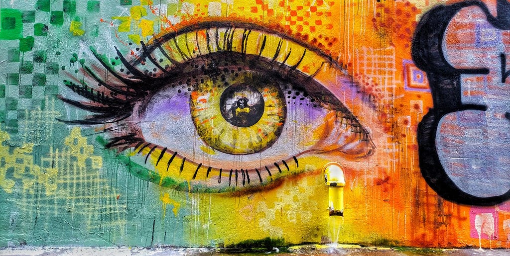 Graffiti eye on a wall in yellow, red and green, with real pipe tear duct.