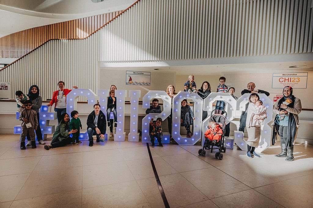 Picture of parents and kids around the CHI 2023 big letters that were in the entrance hall of the conference center.