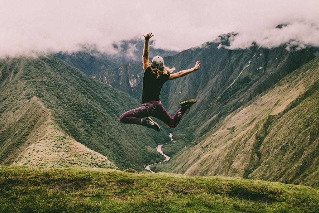 A woman jumping up in the air with mountains and a river in the background