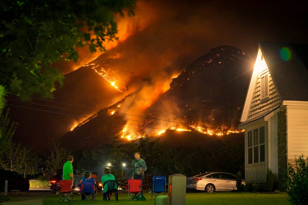 People sit in the back garden of their house watching the hills behind them burning.