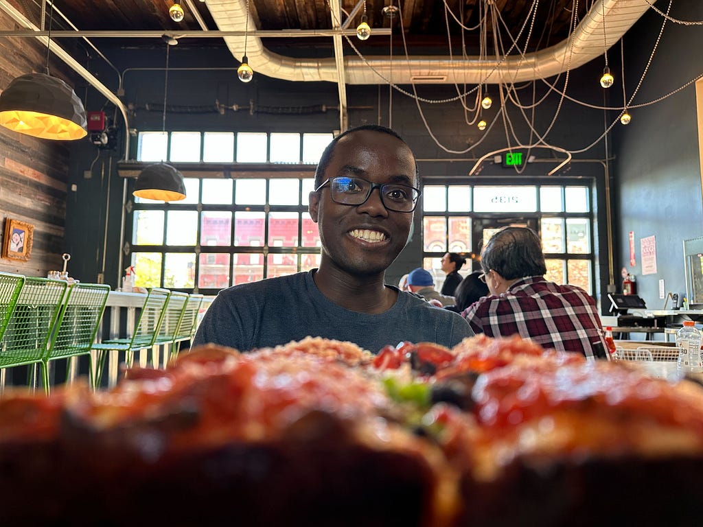 A man smiling while looking at a Detroit-style pizza in an upscale pizza parlor