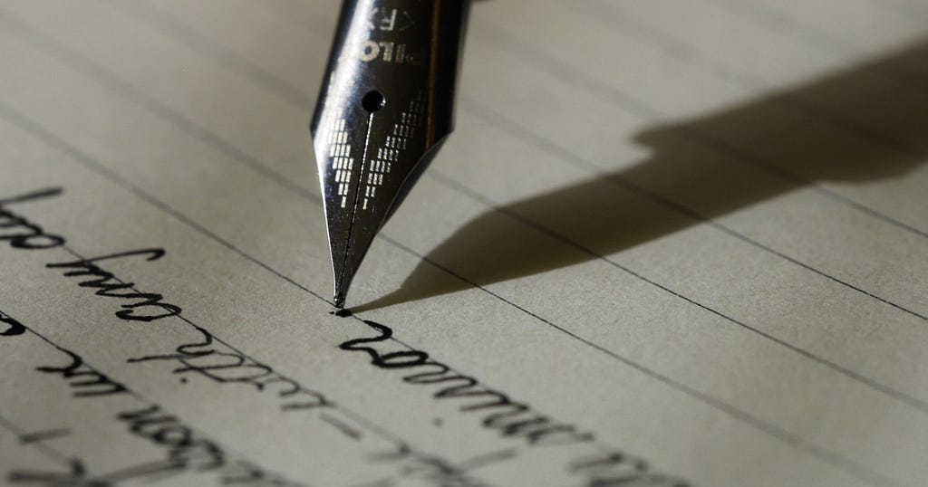 A close-up photo of a fountain pen writing in cursive on lined paper with black ink.