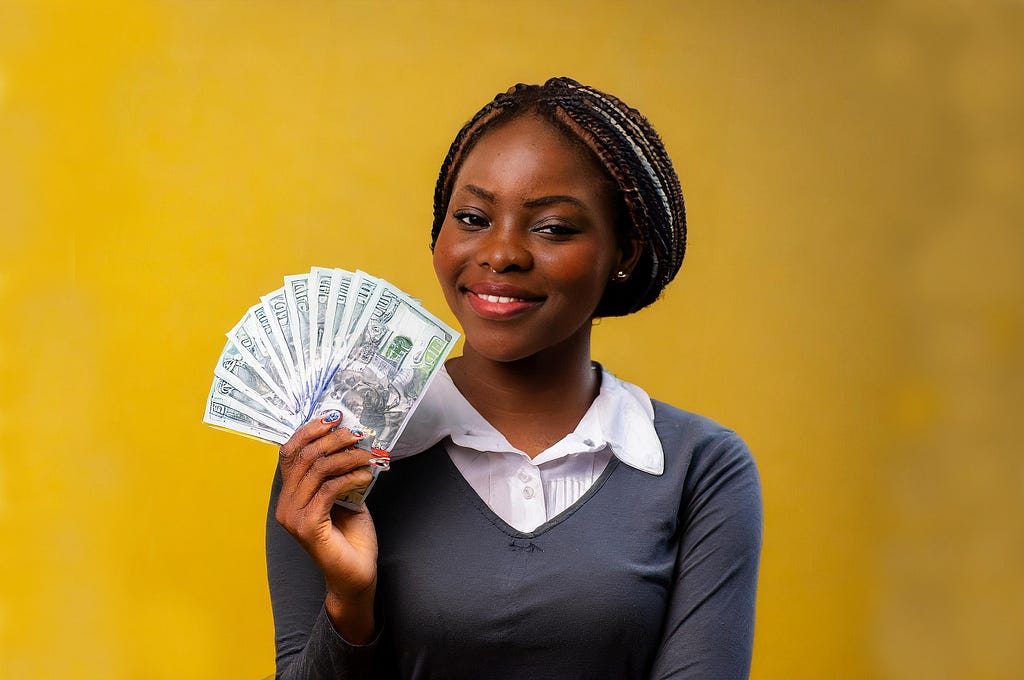 Happy woman holding money in front of a yellow background.