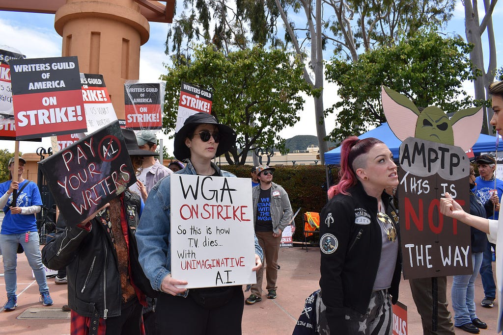 Women on a sidewalk hold “WGA On Strike” Signs