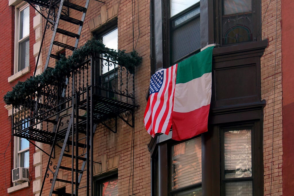 An American flag and Italian flag hang outside of an apartment.