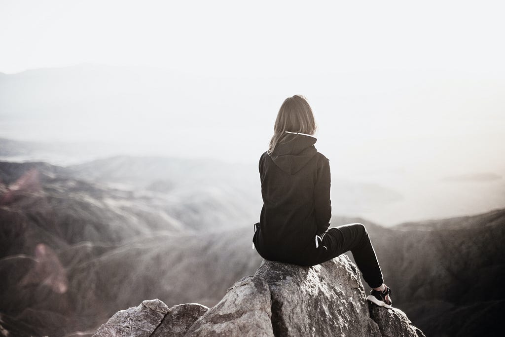 A woman sitting on a mountain top — but with a filter added to make the image darker and colder.