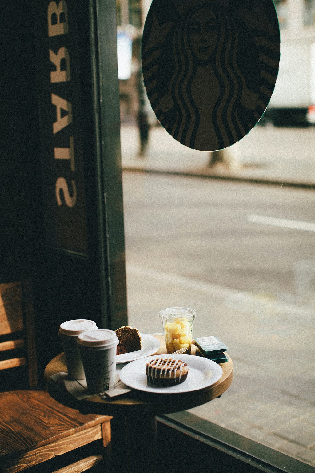 A table in Starbucks with coffees and pastries sitting on it next to a big window looking onto the street.