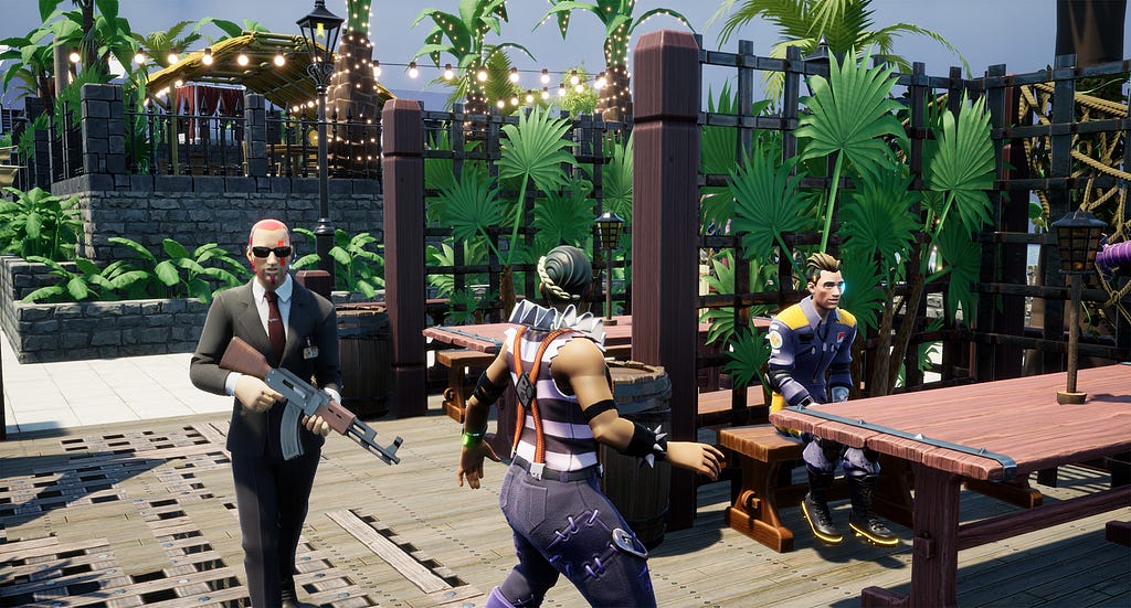 A person in a black suit and holding an assault rifle is walking towards another character outside a seaside restaurant. A third character is sitting at a nearby wooden table.