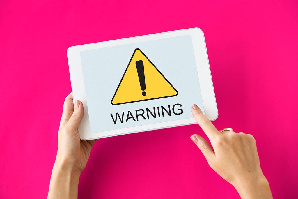 Imagem de uma pessoa segurando um tablet com a mensagem em inglês de “Warning”.