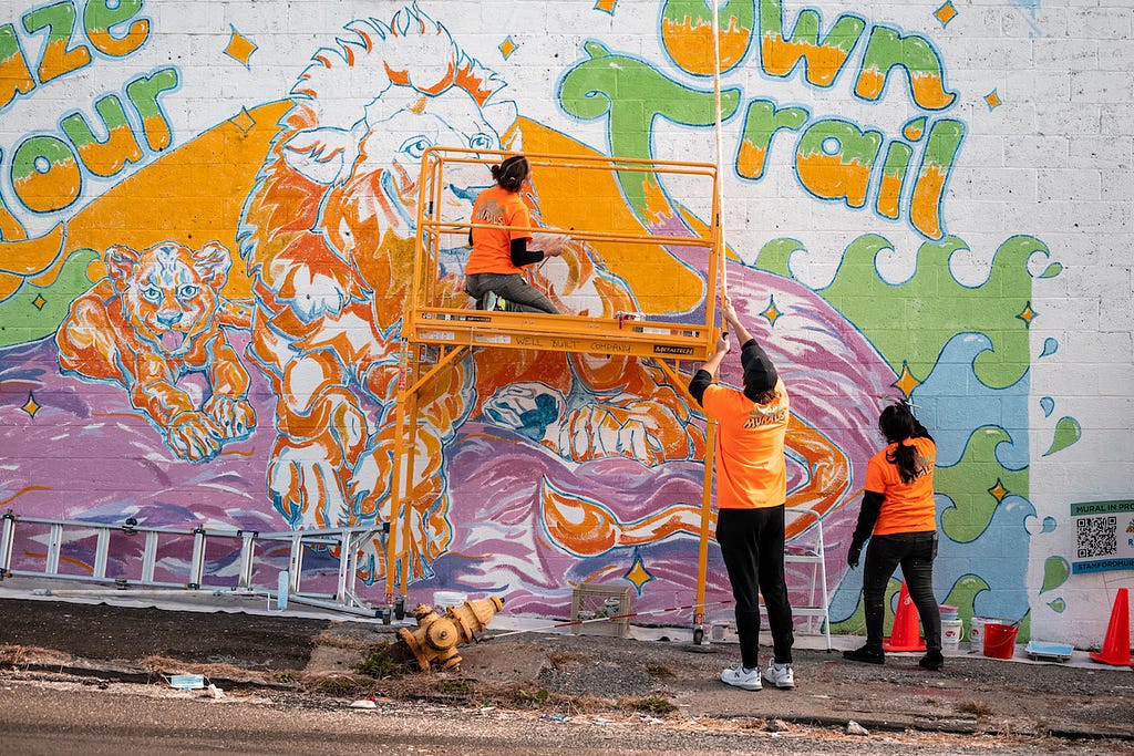 Blaze Your Own Trail mural by artist Alissa Siegal. Collaborators work on the mural featuring the words “Blaze Your Own Trail” with the image of lions and waves surrounding.