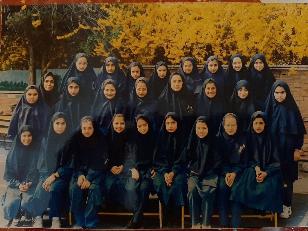 A photo of 10–11 year old girls at school in 1990s. All are wearing dark blue full hijab.
