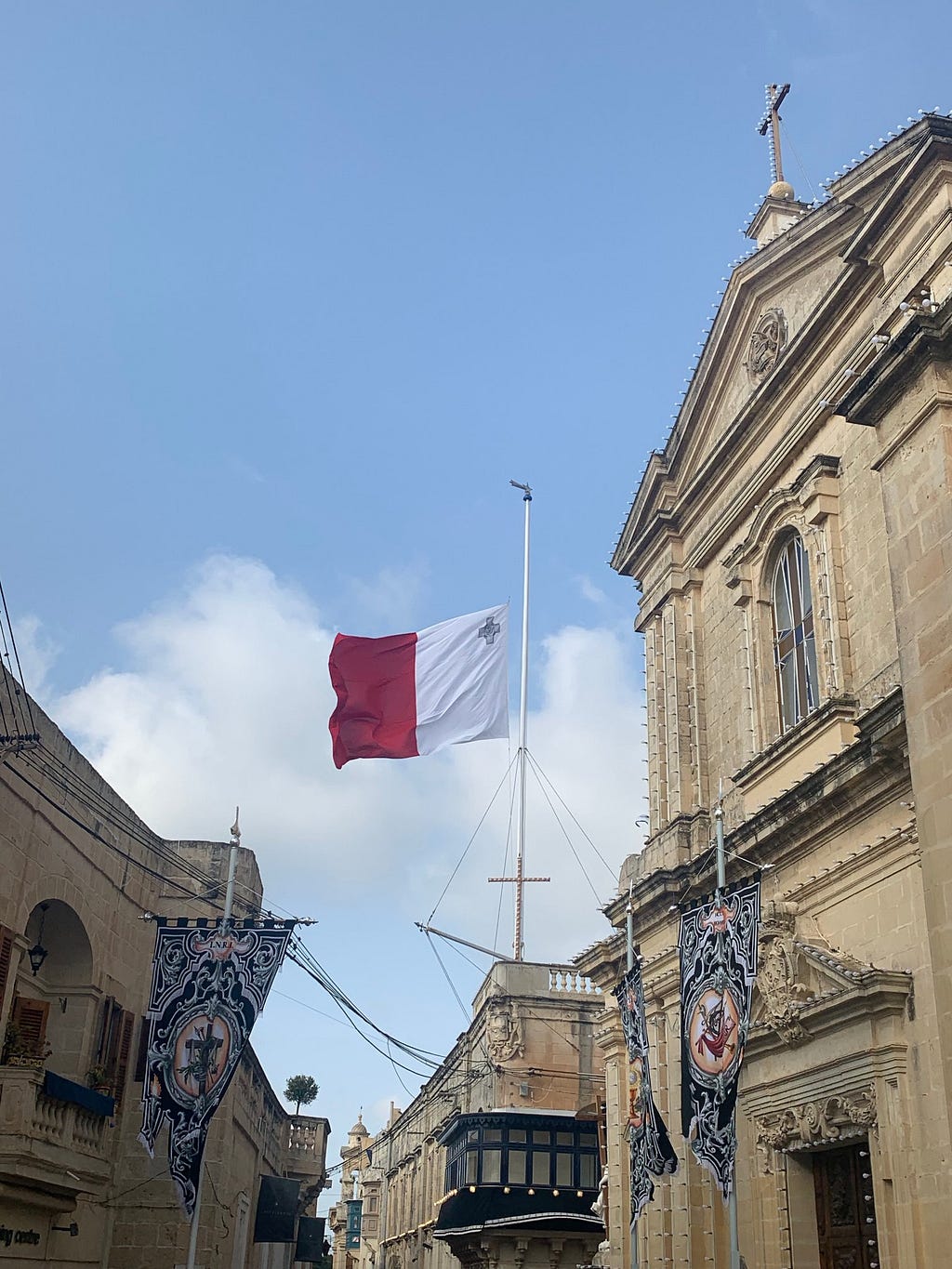 Maltese flag (red and white horizontal stripe with st george cross) flys backwards near a church in Mdina