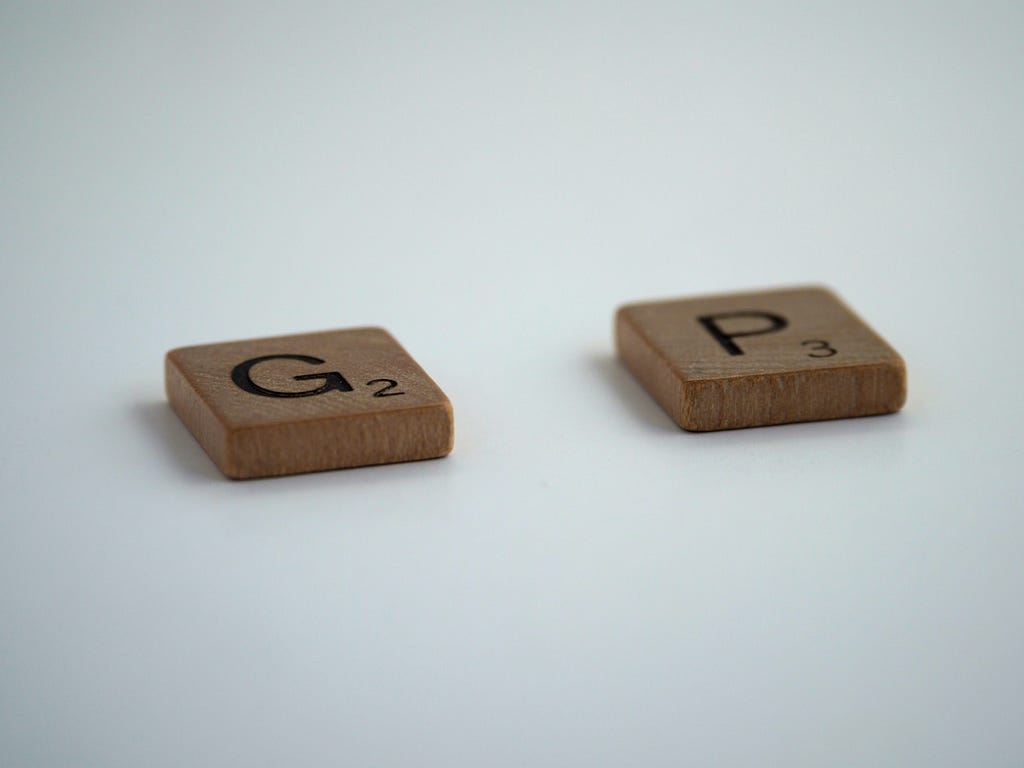 Two tiles/pieces from a Scrabble board game, the letters ‘G’ and ‘P,’ separated from each other by a blank space,