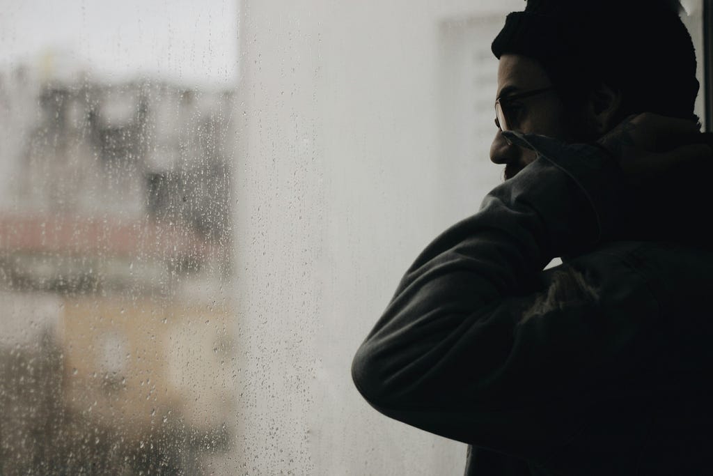 A man staring out through a window as raindrops gather on it.