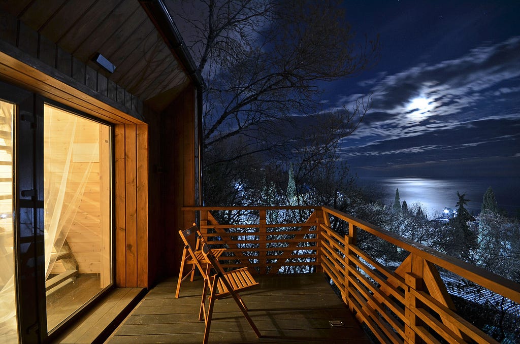 wood chairs on a deck facing moon reflecting off water