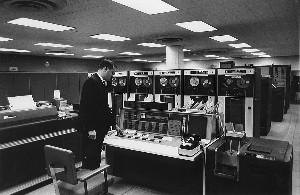 An office worker stood next to a very early, and very large computer in the 1970s.