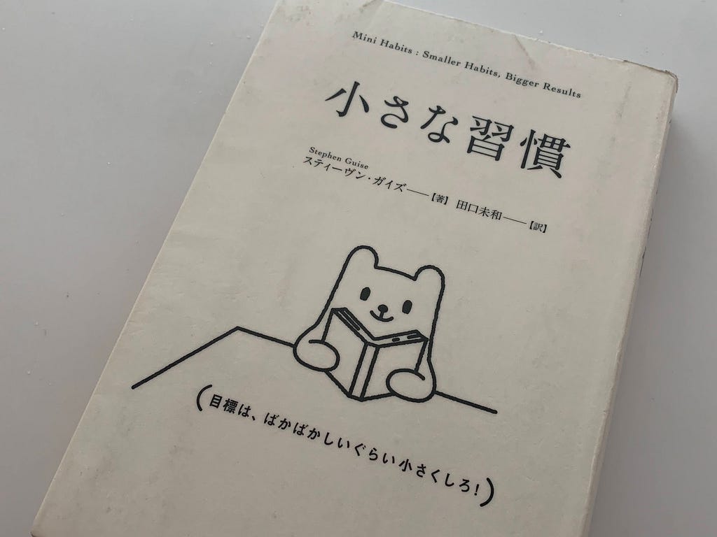 The Japanese edition of the book ‘Mini Habits’ by Stephen Guise, featuring a simple illustration of a smiling bear reading a book.