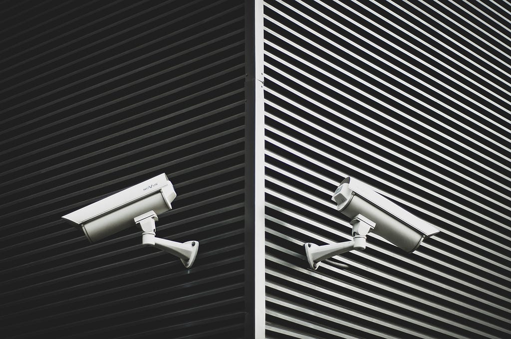Two security cameras on a wall, facing opposite ways.
