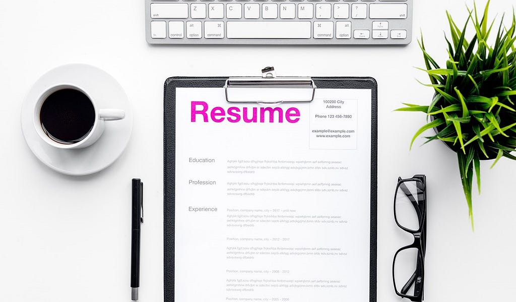 A paper copy of a resume on a clipboard near a keyboard and cup of coffee