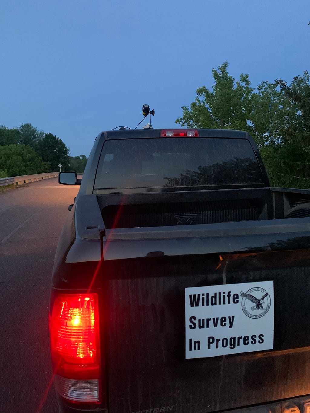 a black truck with a microphone attached to its roof. A bumper sticker on the back of the truck reads “wildlife survey in progress”, with a circular logo of an eagle to the right.