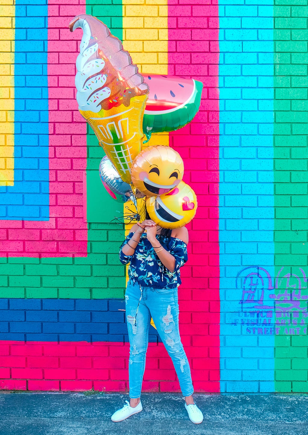 A young girl covering face with smiley balloons with colourful and vibrant background.