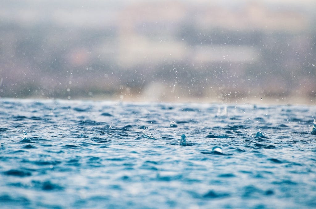 Rain falling onto the surface of a light blue lake.