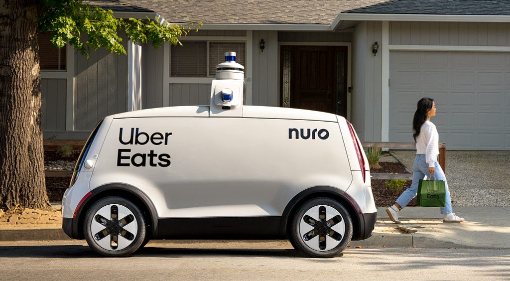 Third generation Nuro vehicle with Uber Eats branding delivering package to young woman.