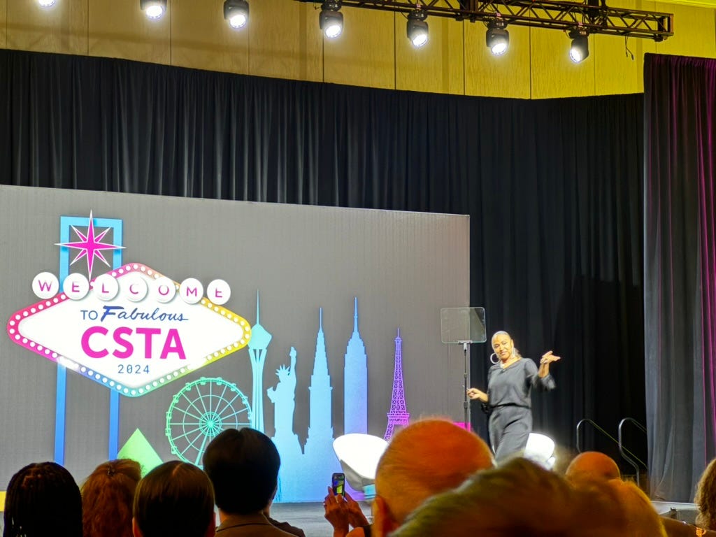 Gholdhy in a black top and bottom gesturing to the audience with the CSTA backdrop.