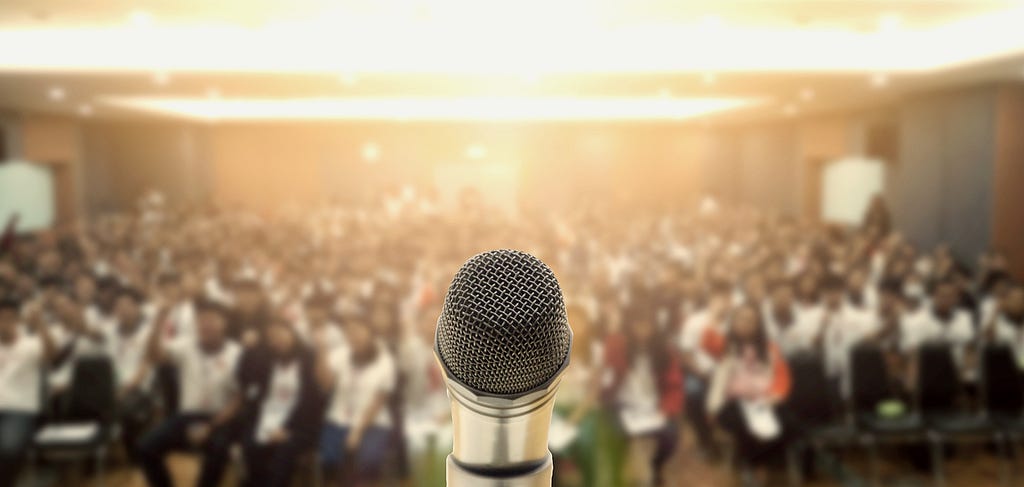 A microphone in the foreground with a large audience in the background.