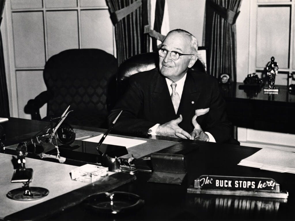 Presidente Harry Truman em sua mesa com a placa "The Buck Stops Here"