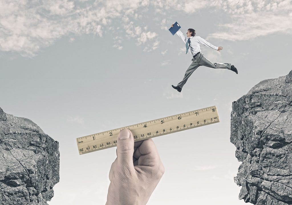 Business guy jumping over chasm with a giant hand holding a ruler so he doesn’t fall.