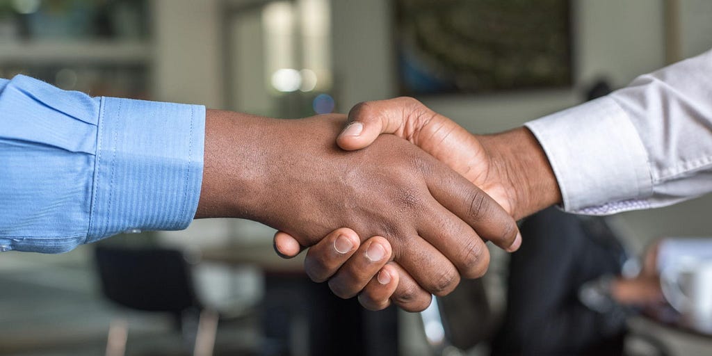 A closeup of two Black men’s hands clasped in the most perfect of greetings in an office setting