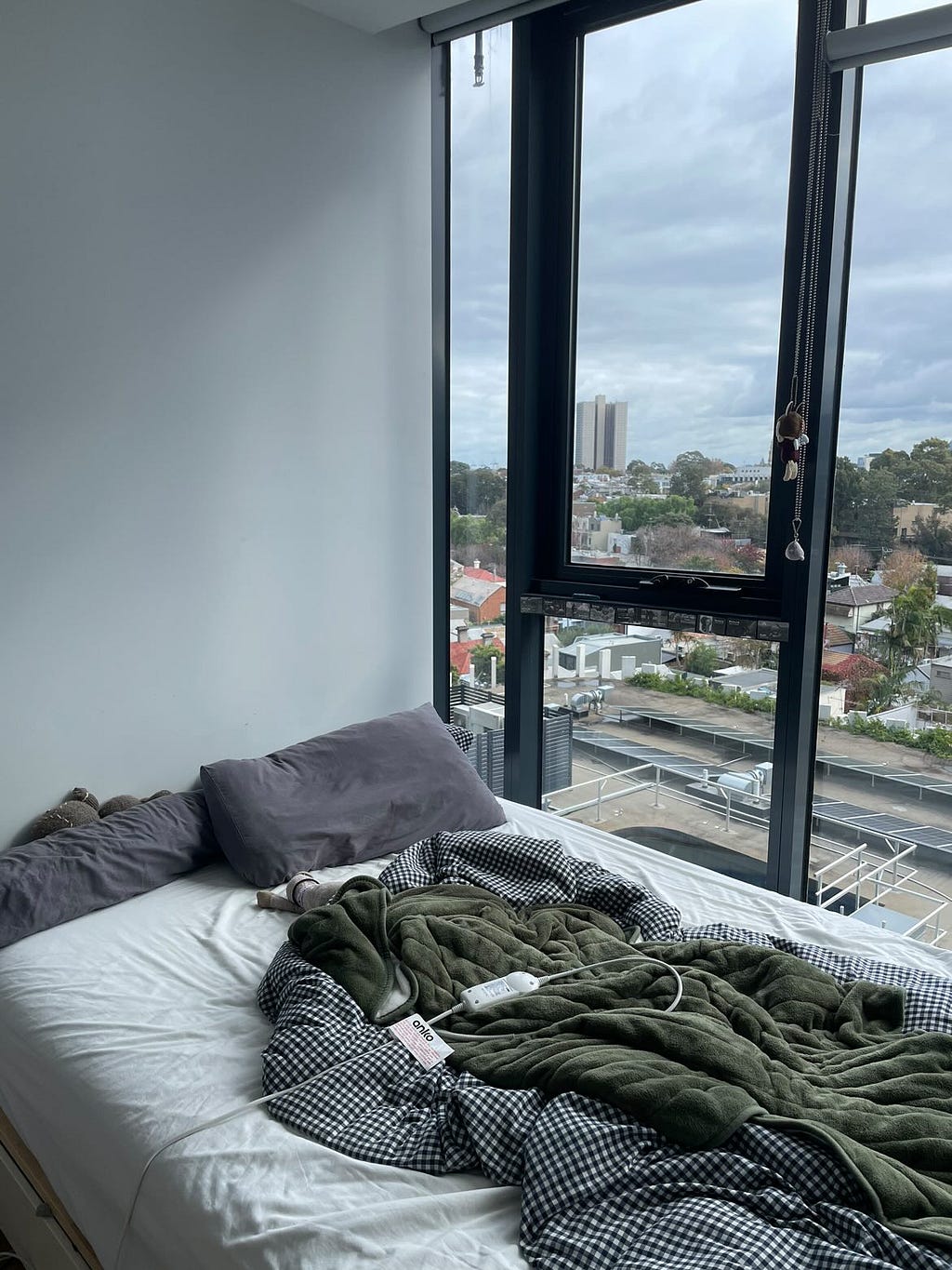 Photo of a bed with messy blankets and a big window looking out into the city.