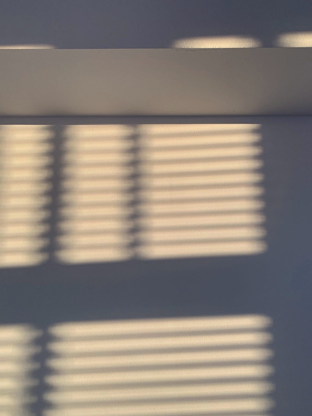 Sunlight filtered through window blinds falling across a blank wall.