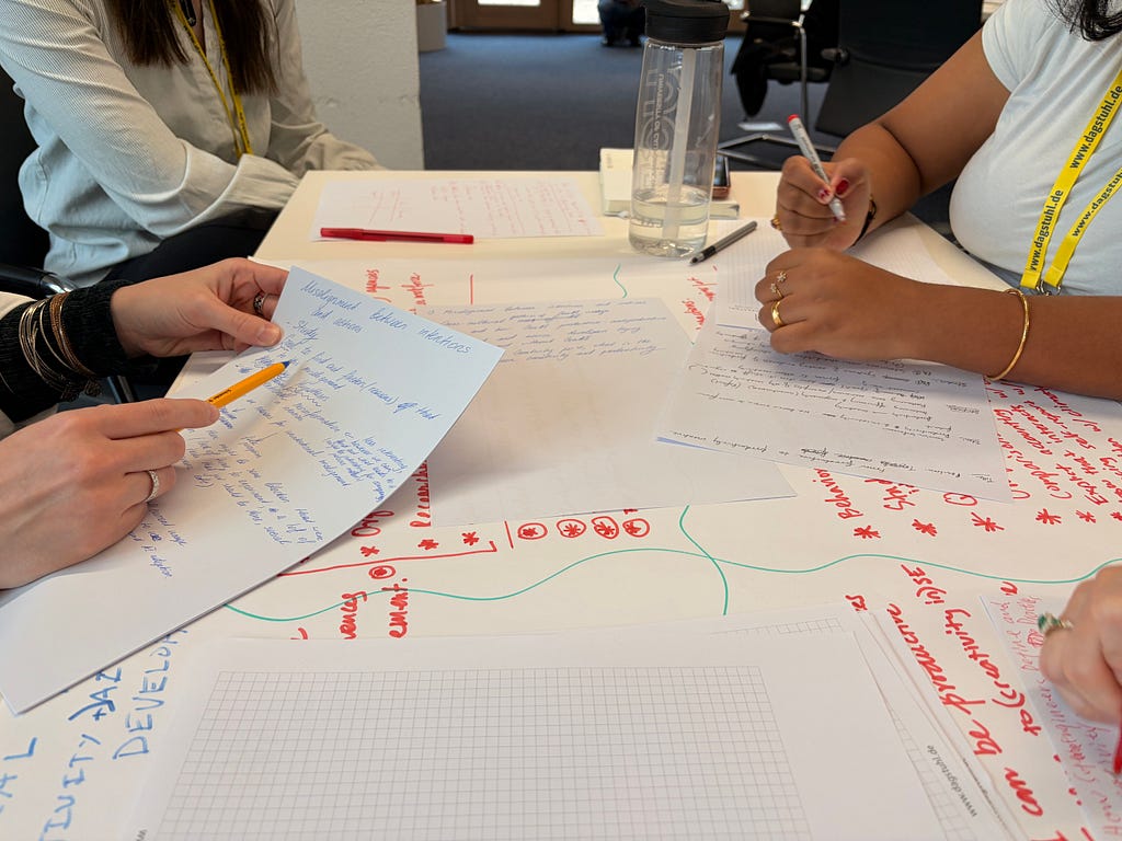 Paper and ink and writing splattered across a table with human hands gesturing and writing.