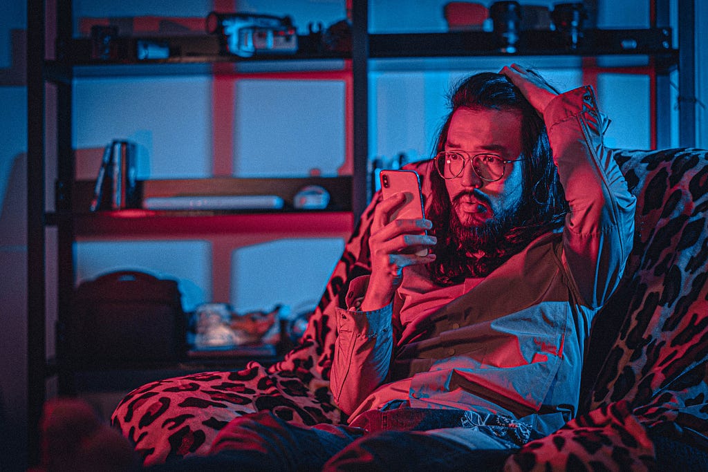 A concerned ethnic man watching smartphone on cozy armchair at home