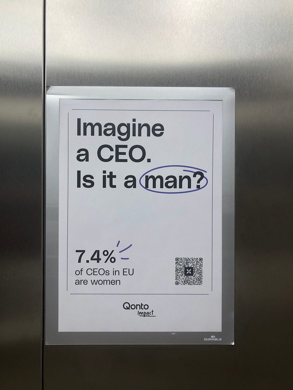 Poster on an elevator wall with an eye-catching headline: “Imagine a CEO.” The next line reads: “Is it a man?” The final line reads: “7.4% of CEOs in EU are women”. The poster is signed “Qonto Impact”.