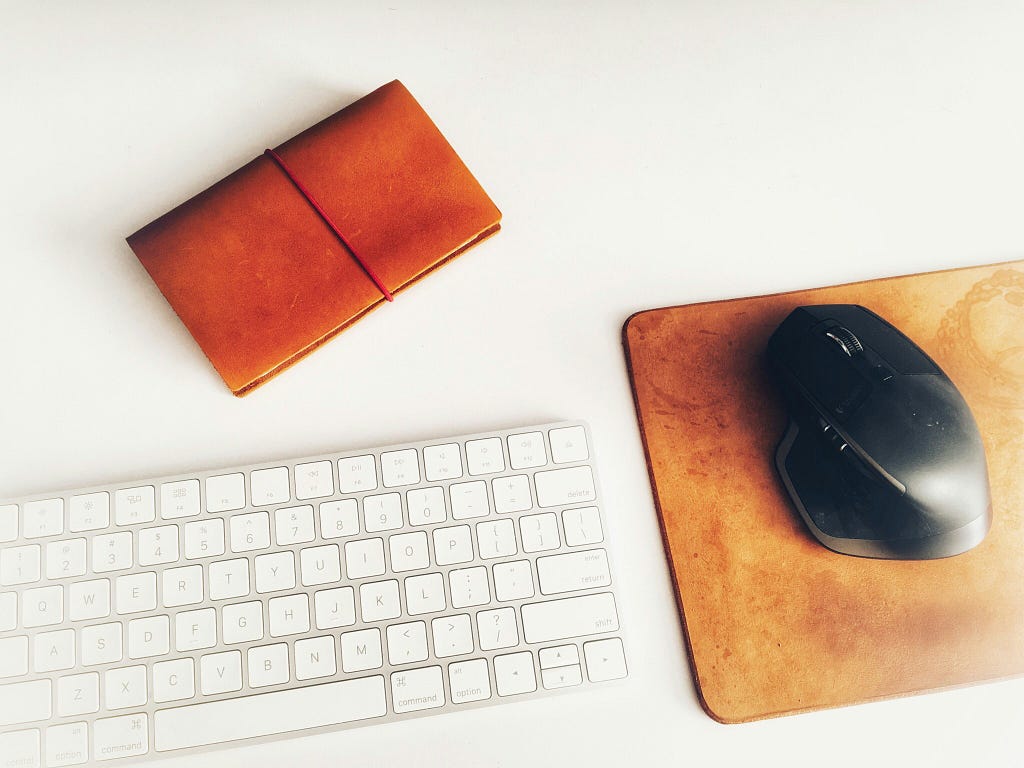 Computer mouse, keyboard, and notebook on a white desk