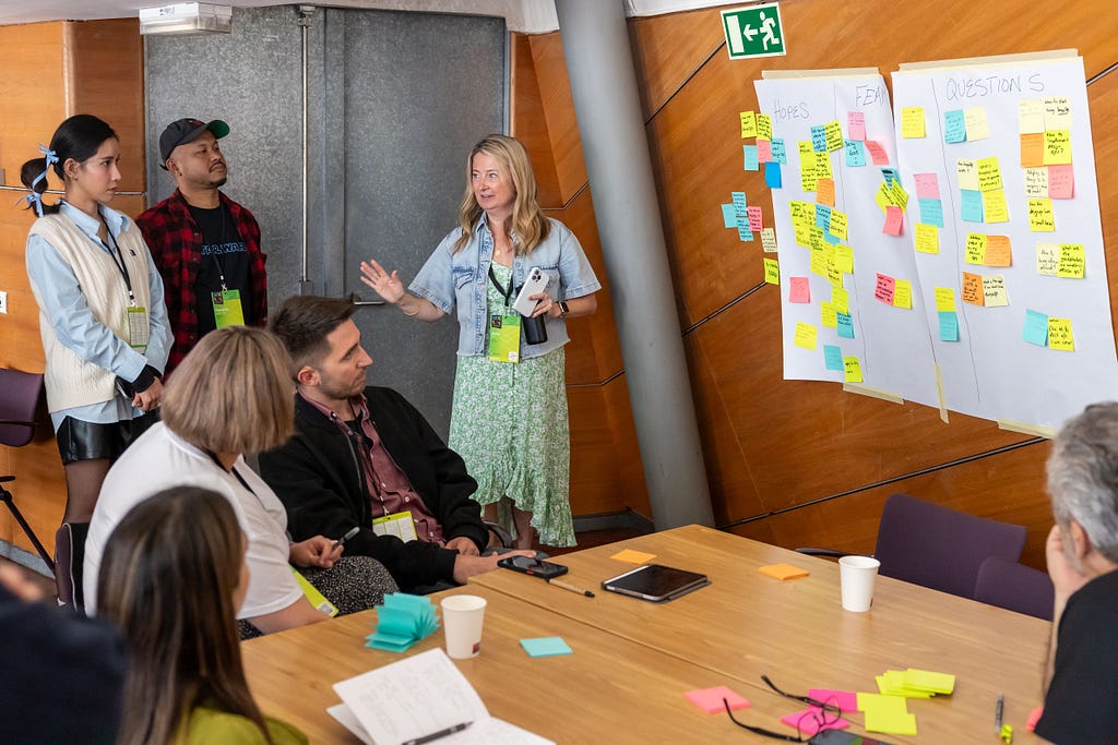 Jenny explaining something to the attendees, who are looking at a wall with post-its.