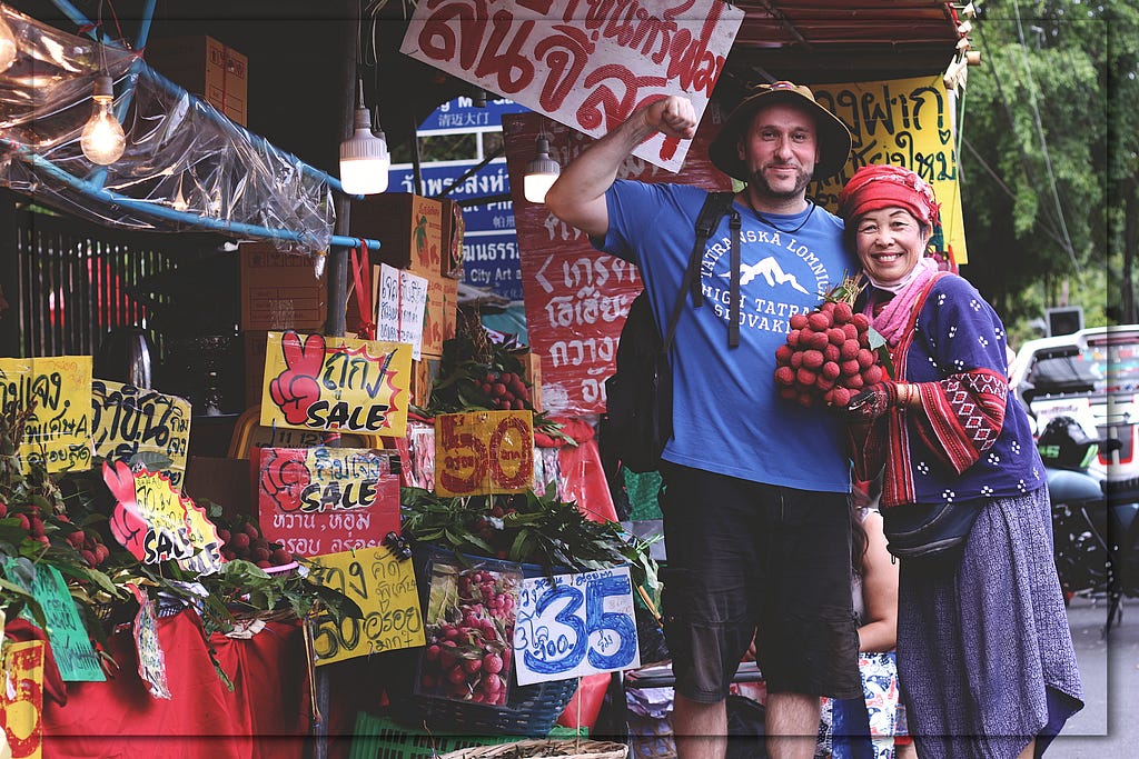 A photograph of me with a local Thai woman selling lychees at an outdoor market. She is dressed in traditional clothing.