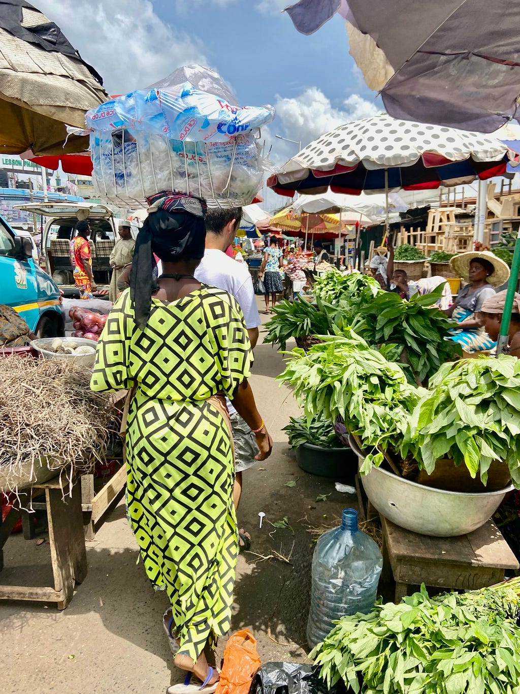 A woman from the back in a market, carrying a package on her head