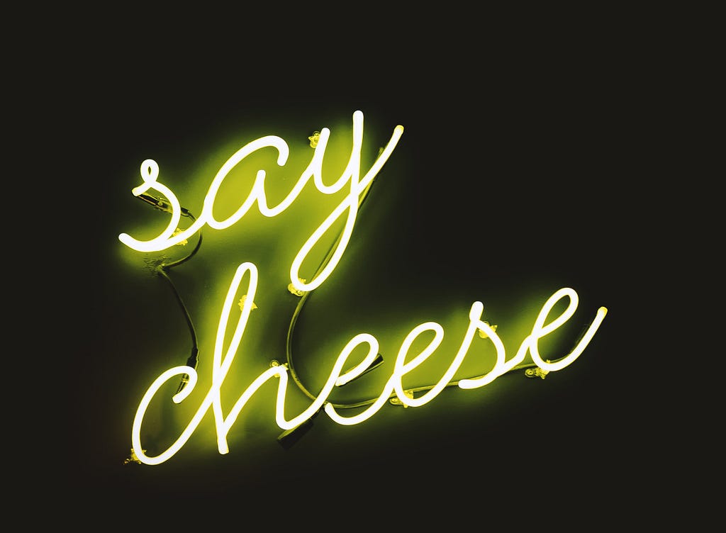 A neon yellow sign saying ‘say cheese’ on a black background.