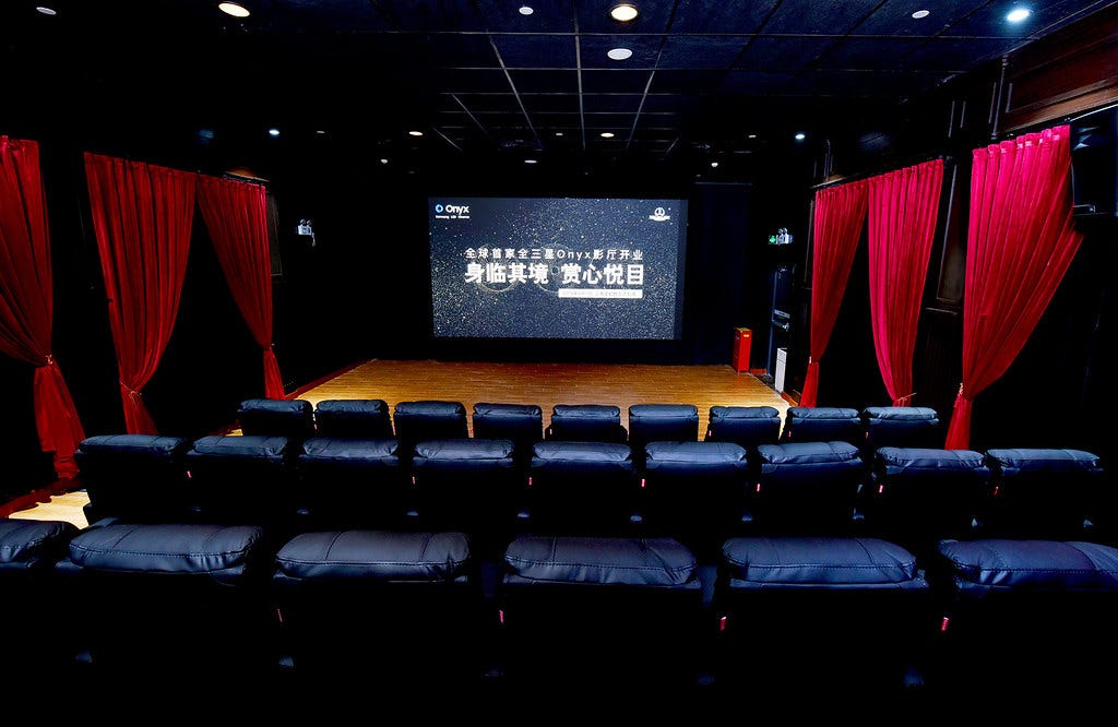 Sala de cinema com luzes acessas e escritas em mandarim na tela.