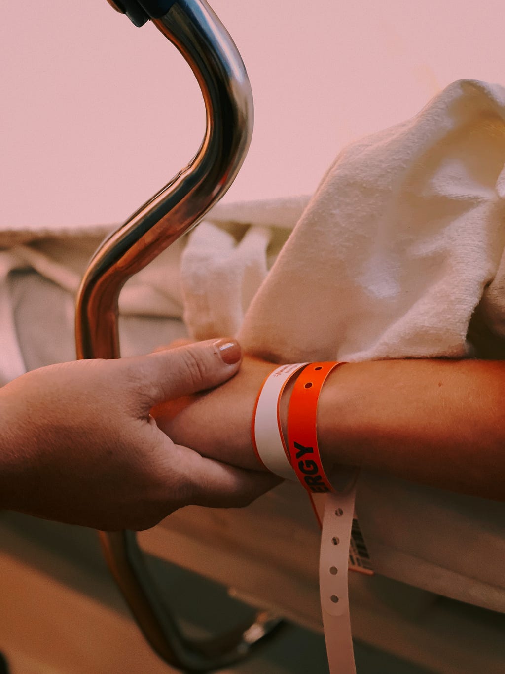 a patient’s hand, with hospital wrist bands on, being held by another person’s hand.