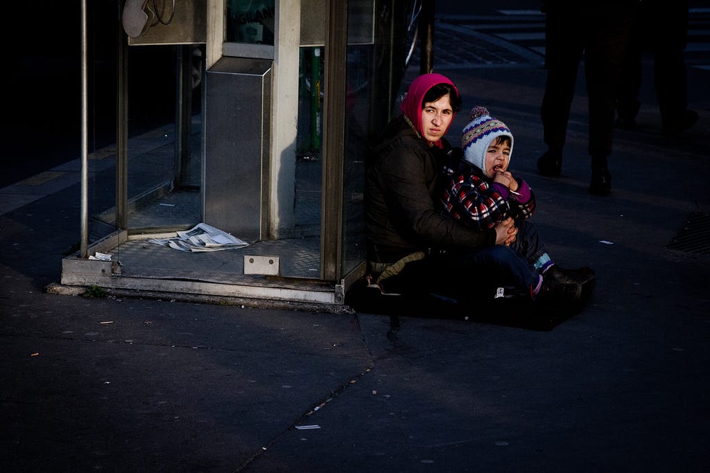 Woman holding a kid on the streets of Paris begging for money.