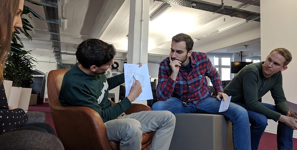 Three people observing what one person has created and is now presenting in a workshop.